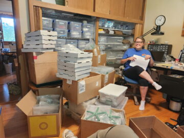 An office space cluttered with many boxes and crammed with items on shelves.